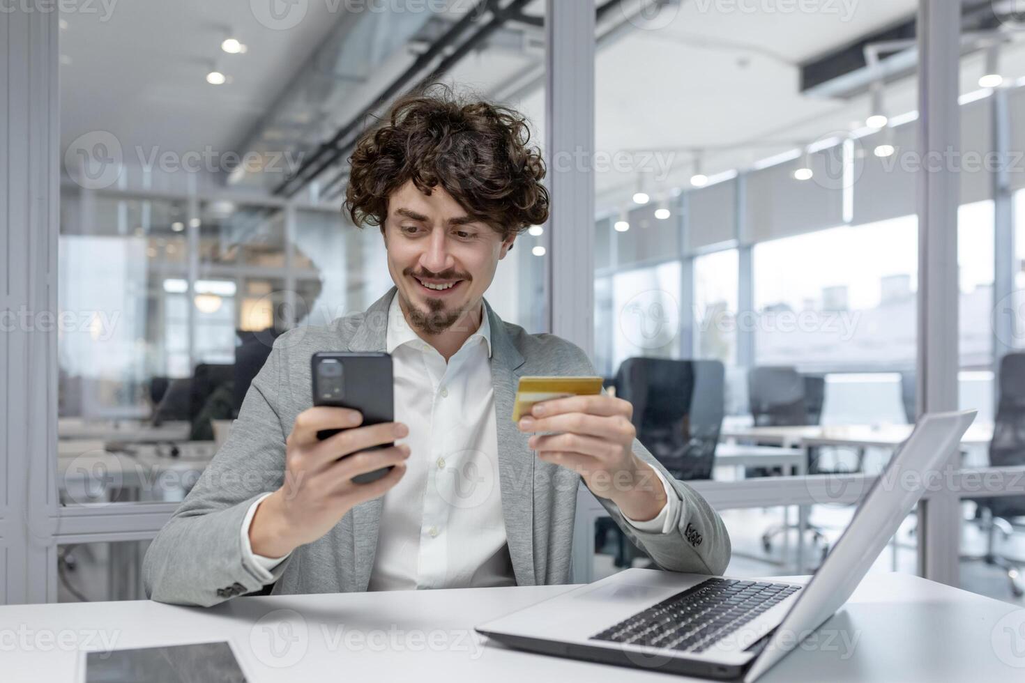 esperto giovane adulto uomo d'affari nel un' moderno ufficio, sorridente come lui usi un' Telefono. Spettacoli multitasking, messa a fuoco, e un' positivo emotivo stato. foto