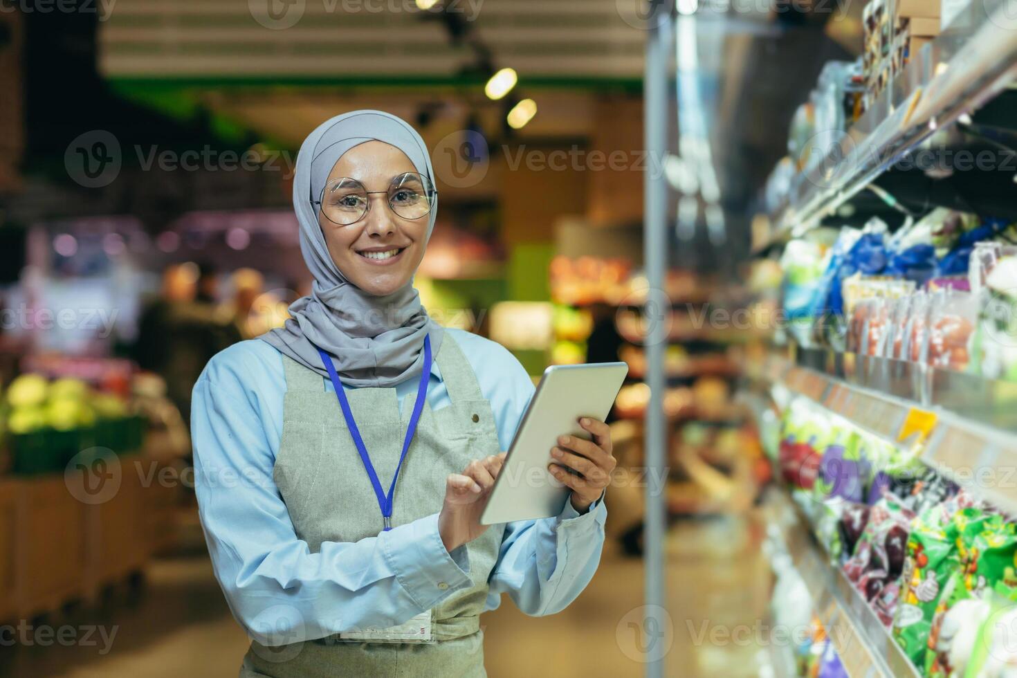 ritratto di contento e sorridente venditore donna nel hijab, musulmano donna con tavoletta sorridente e guardare a telecamera, commessa vicino campo con verdure e insalata prodotti sceglie e setaccia termine foto