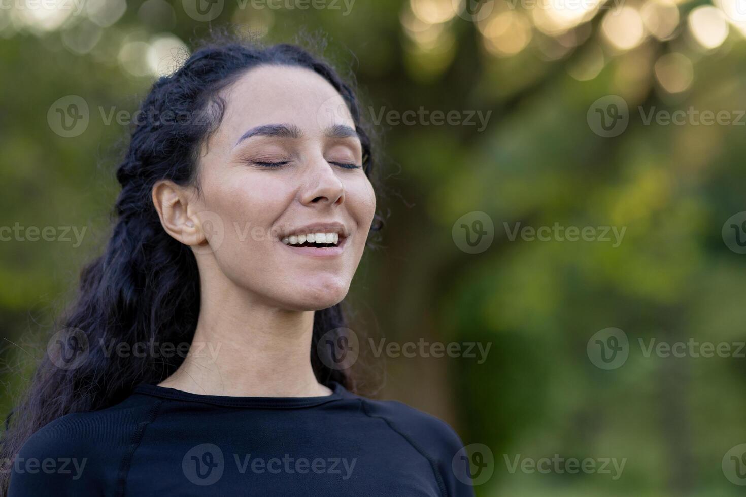 un' ispanico donna si chiude sua occhi con un' soddisfare Sorridi, crogiolarsi nel serenità in mezzo un' naturale verde sfondo. foto