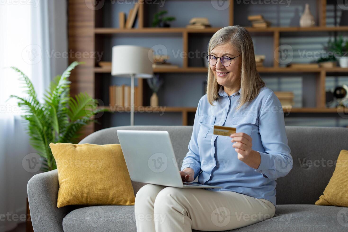 maturo donna con bicchieri utilizzando un' il computer portatile e credito carta su un' accogliente divano. concetto di in linea shopping e commercio elettronico. foto