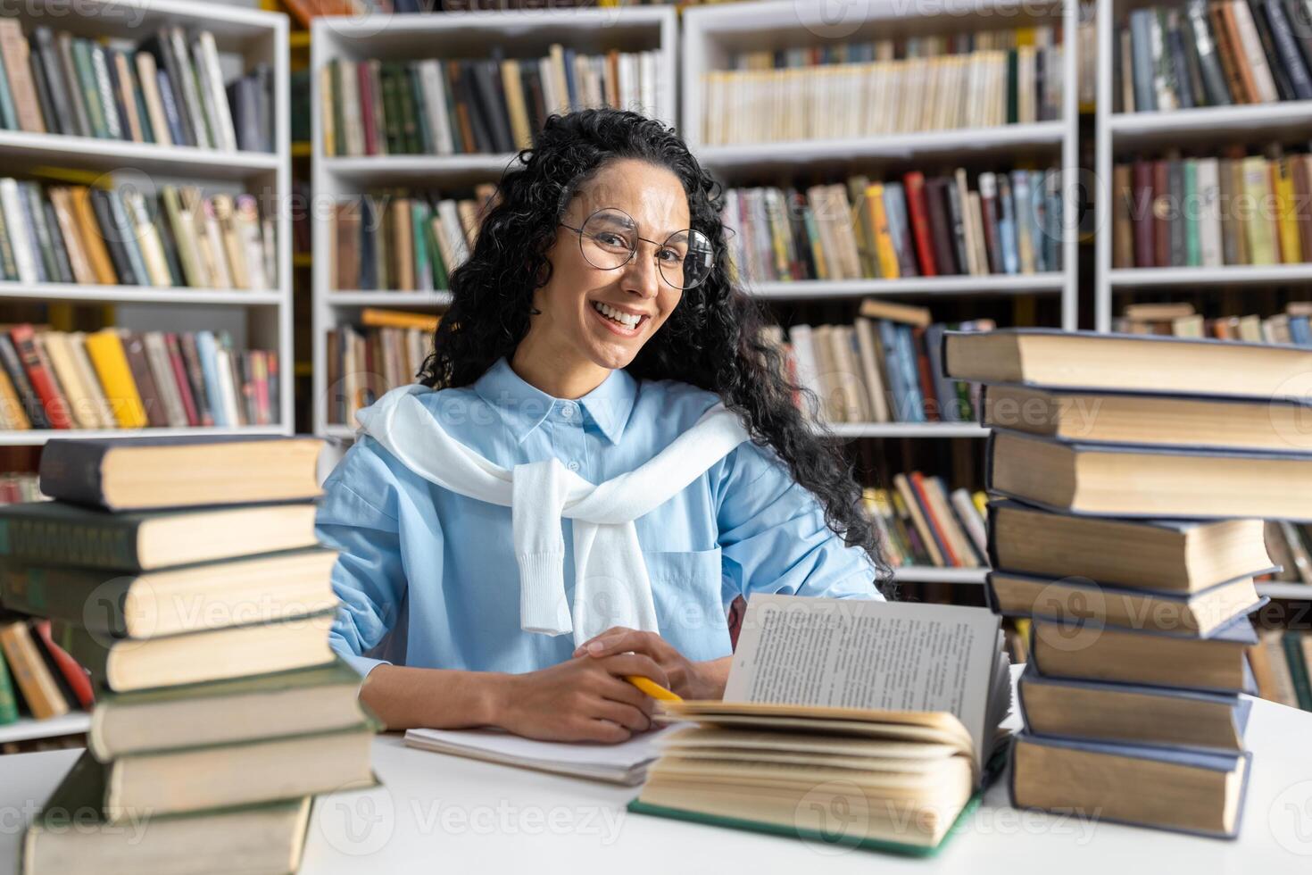 un' allegro giovane donna con bicchieri e Riccio capelli studi tra pile di libri nel un' biblioteca, trasudante curiosità e entusiasmo. foto