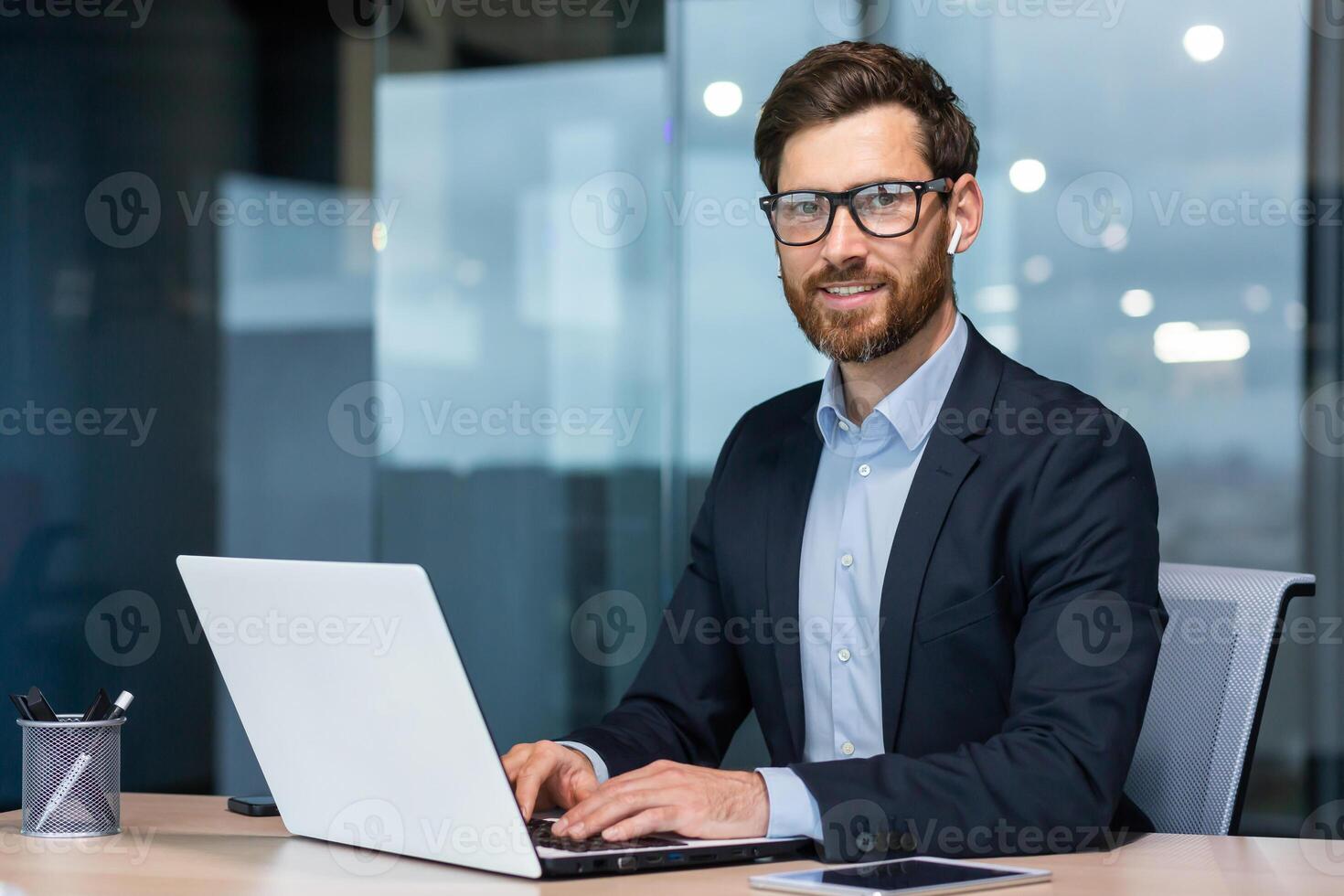 ritratto di maturo riuscito e contento uomo d'affari, anziano uomo con barba sorridente e guardare a telecamera, investitore Lavorando con il computer portatile dentro ufficio nel attività commerciale completo da uomo. foto