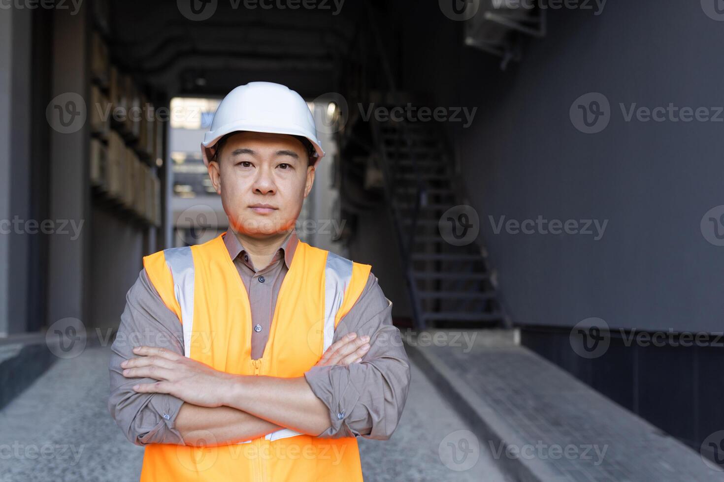 ritratto di un asiatico giovane uomo chi lavori nel costruzione e produzione, in piedi nel un' protettivo casco e veste, attraversamento il suo braccia su il suo le spalle, guardare con fiducia a il telecamera. foto