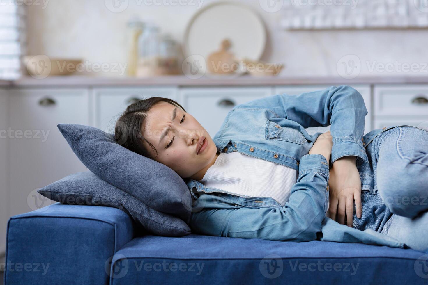 giovane bellissimo donna malato solo a casa dire bugie su letto, asiatico ragazza Tenere mani su stomaco foto