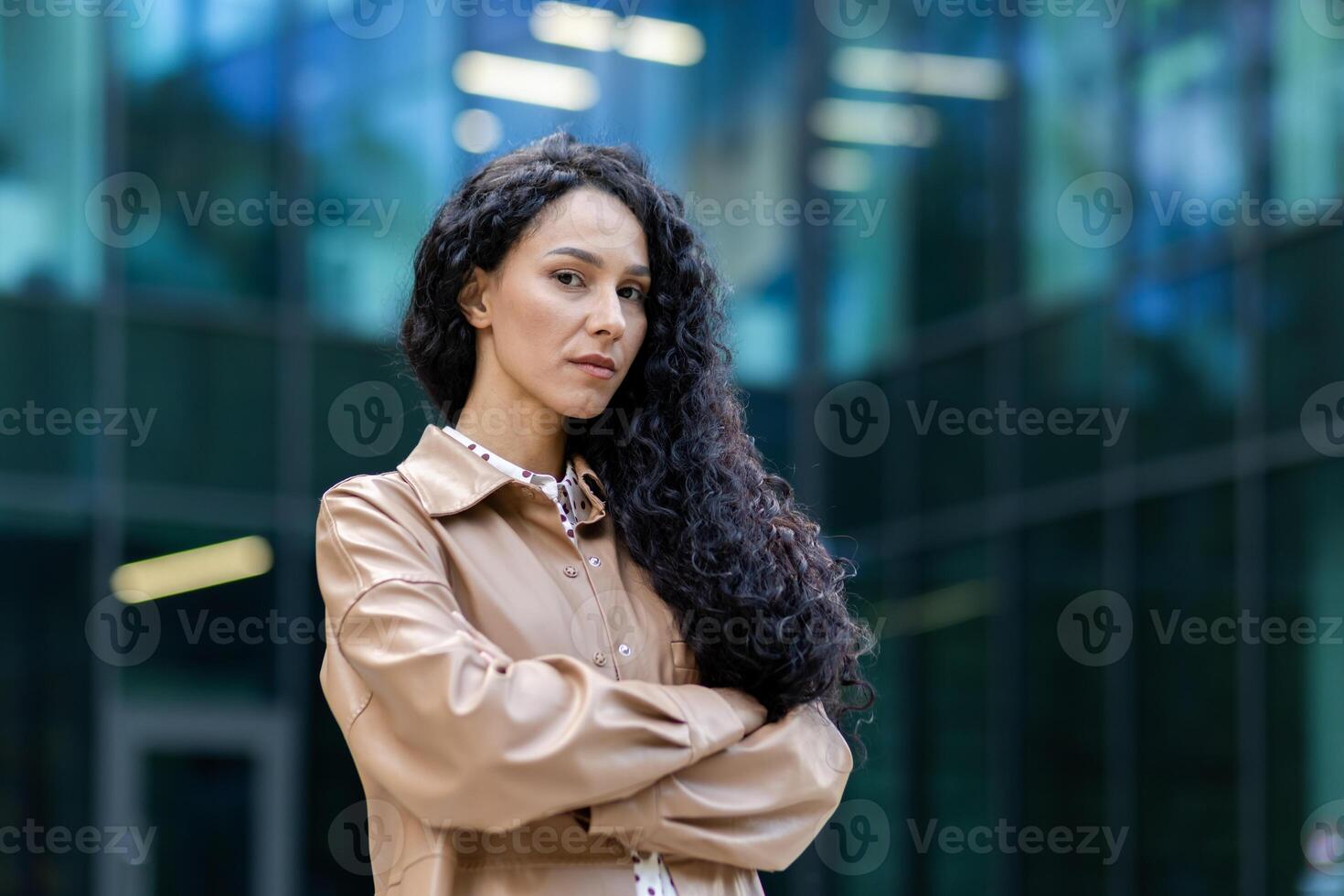 ritratto di riuscito orgoglioso donna capo al di fuori ufficio costruzione, ispanico soddisfatto con opera guardare a telecamera con attraversato braccia, maturo donna d'affari con Riccio capelli in piedi e in posa. foto