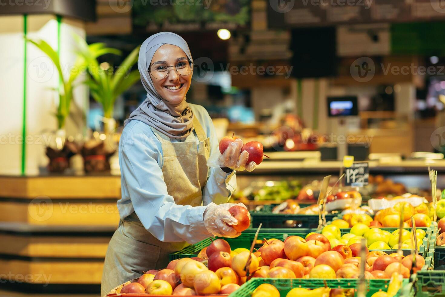 un' giovane bellissimo hijabi musulmano donna, un' supermercato lavoratore, stabilisce frutta nel il Dipartimento foto