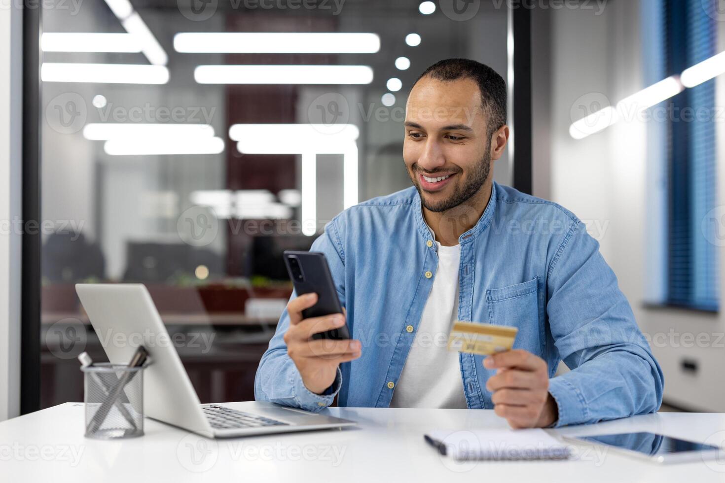 un' persona coinvolgente nel in linea shopping utilizzando un' credito carta e smartphone a un' contemporaneo ufficio spazio di lavoro. foto