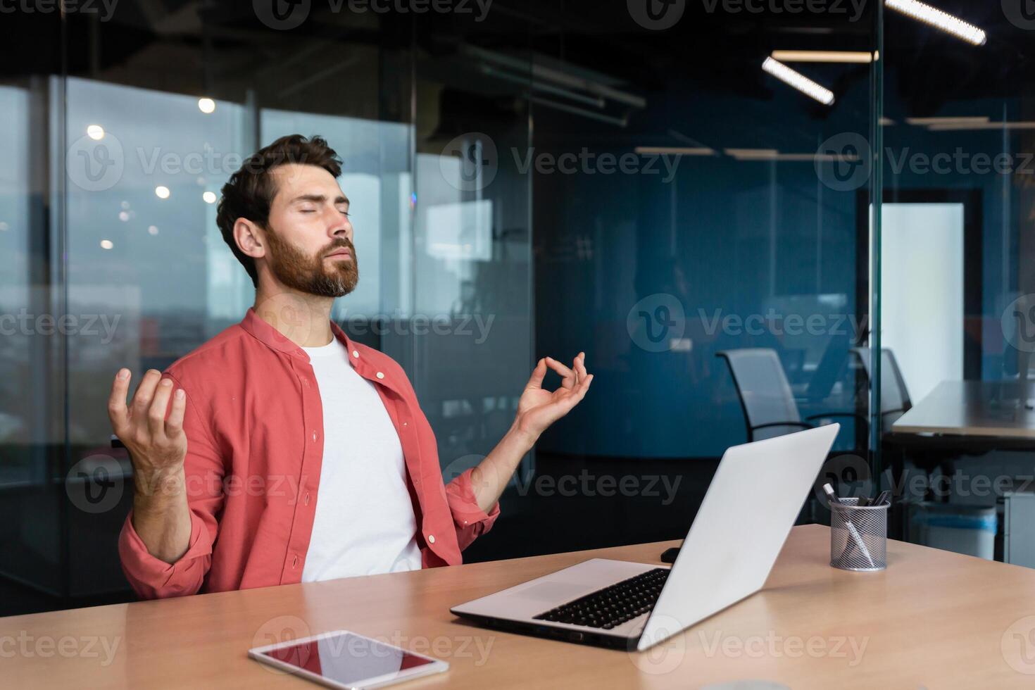 uomo d'affari nel un' camicia riposo e Meditare nel il ufficio nel il loto posizione, un' uomo a il posto di lavoro rilassa durante il giorno seduta a il posto di lavoro con un' il computer portatile con il suo occhi Chiuso. foto