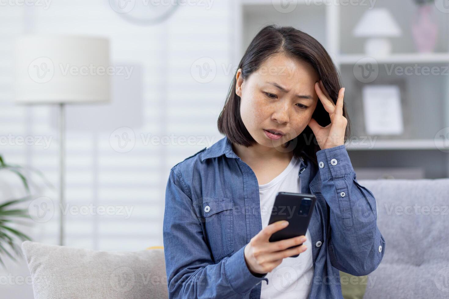 giovane asiatico donna irritato seduta a casa, donna avuto cattivo notizia in linea su Telefono seduta su divano nel vivente camera, irritato e deluso. foto