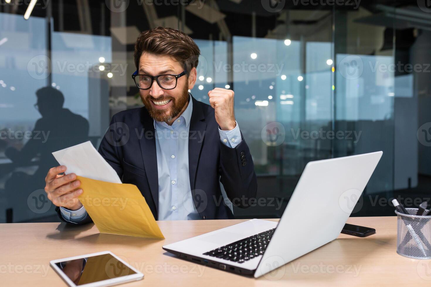 maturo uomo d'affari contento con bene notizia ricevuto lettera nel Busta, anziano uomo con barba lettura e sorridente Lavorando dentro ufficio a opera utilizzando computer portatile, investitore festeggiare realizzazione vittoria. foto