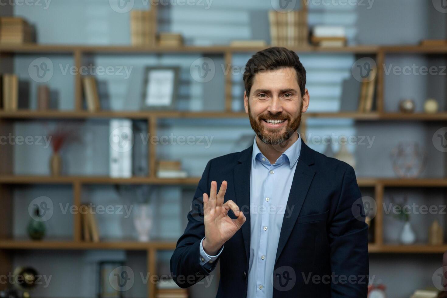 professionale maturo maschio attività commerciale proprietario mostrando positivo approvazione con un va bene mano cartello nel un' ben organizzato ufficio ambientazione. foto