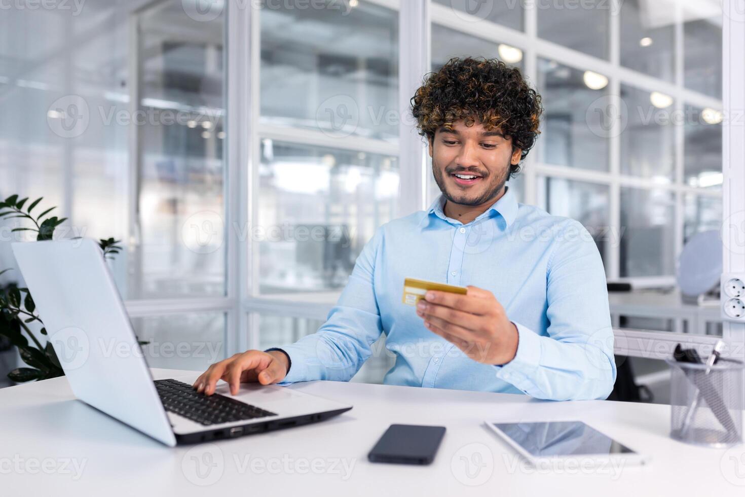 giovane ispanico uomo d'affari seduta nel ufficio, Lavorando su il computer portatile e utilizzando credito carta. paga, controlli il account, conduce il transazione. foto