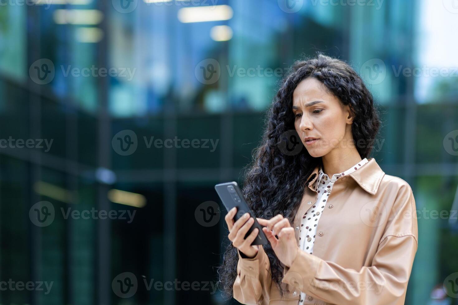 irritato e triste donna con Telefono nel mani lettura in linea Messaggio, ispanico attività commerciale donna ricevuto cattivo notizia notifica mentre a piedi al di fuori ufficio edificio con smartphone. foto