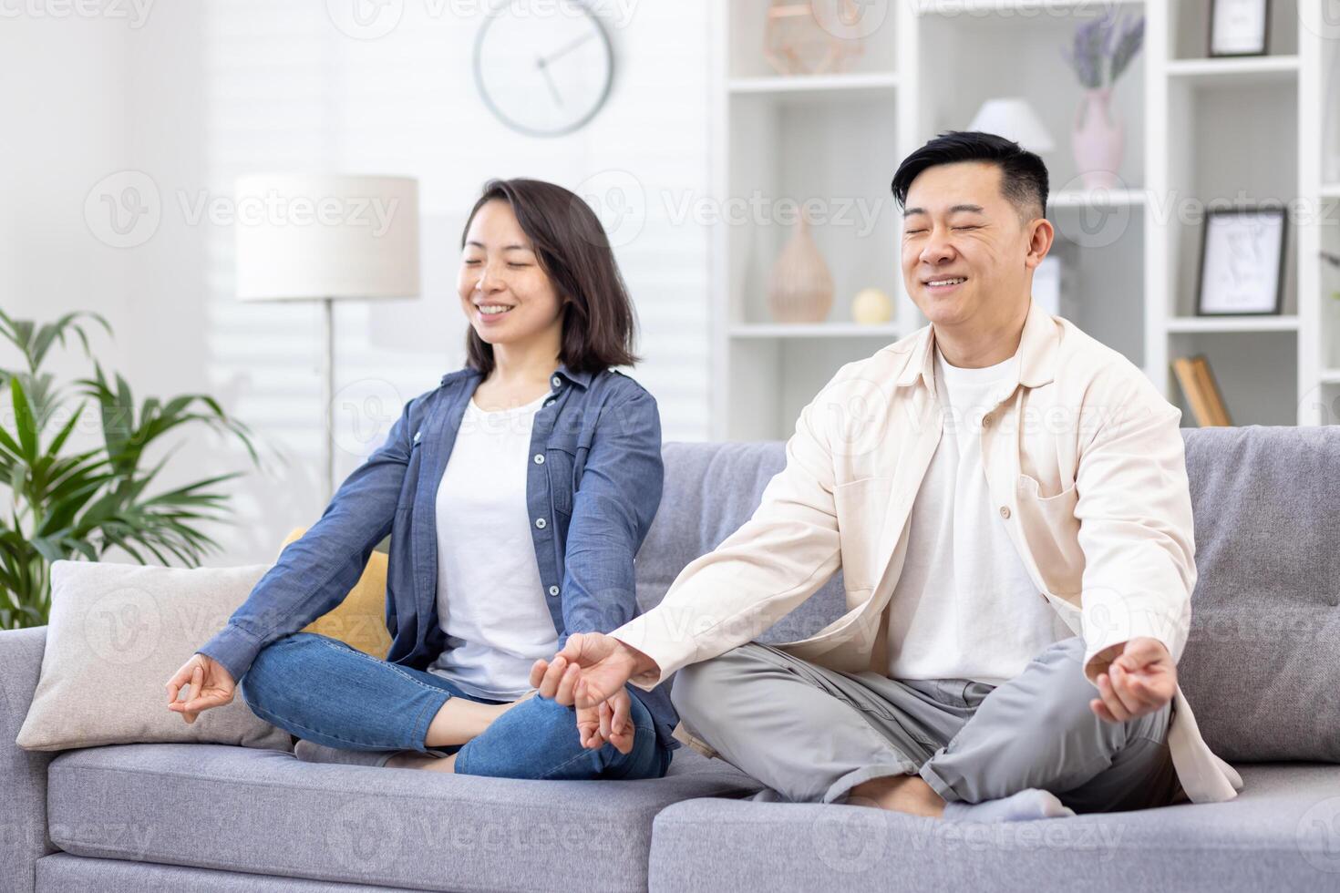 giovane asiatico giovane famiglia, coppia, uomo e donna trascorrere tempo insieme, riposo, fare yoga. essi siamo seduta su il divano nel il loto posizione con loro occhi Chiuso, sorridente, rilassante. foto