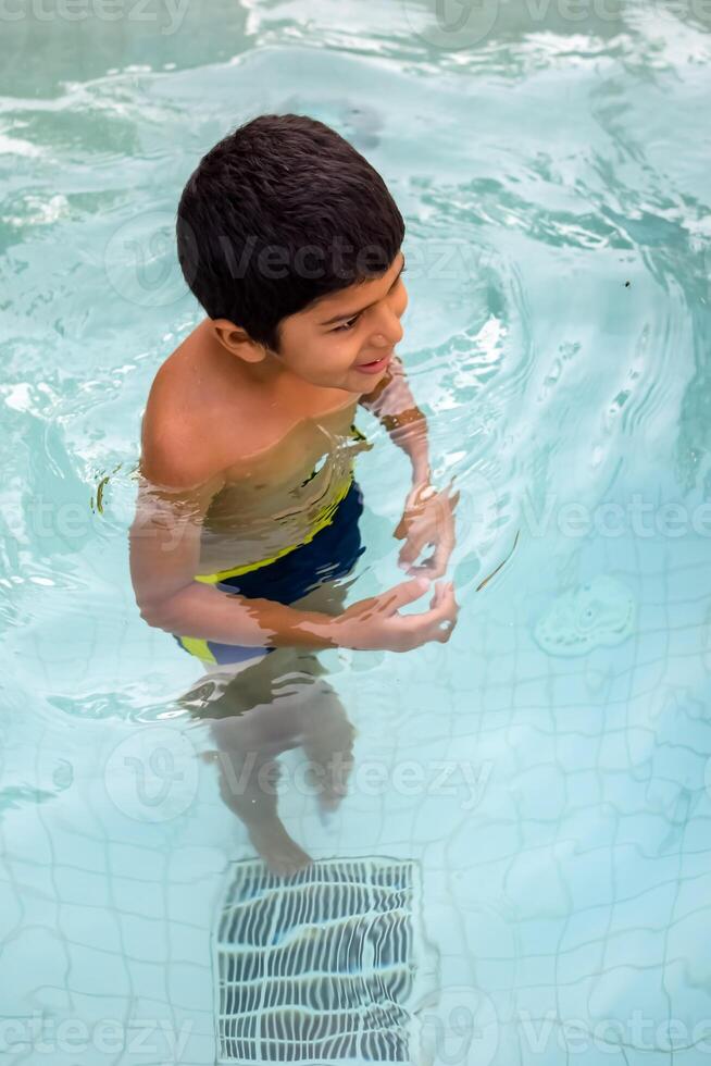 contento indiano ragazzo nuoto nel un' piscina, ragazzo indossare nuoto costume lungo con aria tubo durante caldo estate vacanze, bambini ragazzo nel grande nuoto piscina. foto