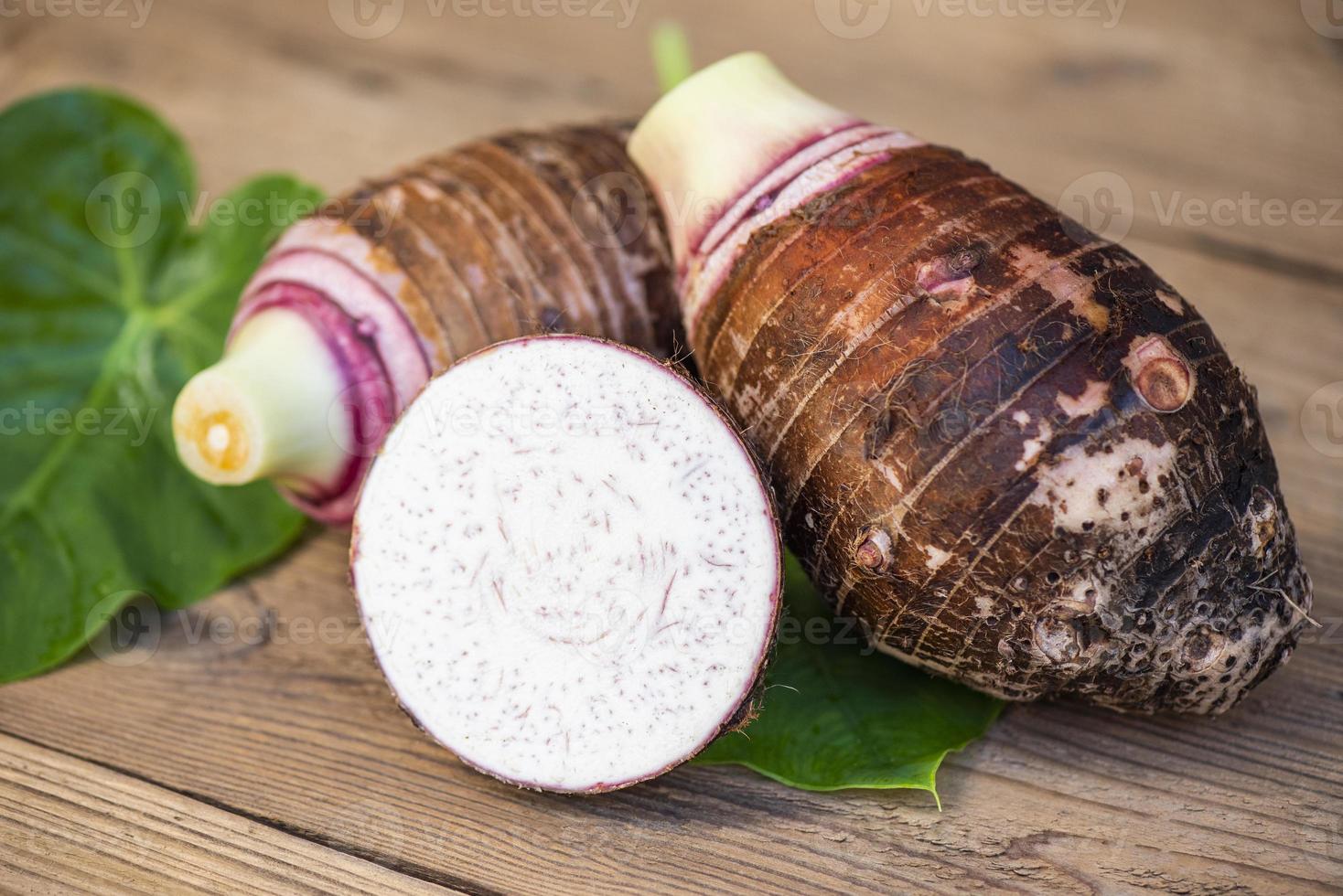 radice di taro con mezza fetta su foglia di taro e fondo in legno, radice di taro organica cruda fresca pronta da cucinare foto