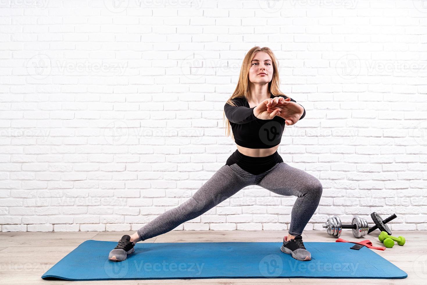 Giovane donna in forma che fa affondi laterali al chiuso su un tappetino fitness foto