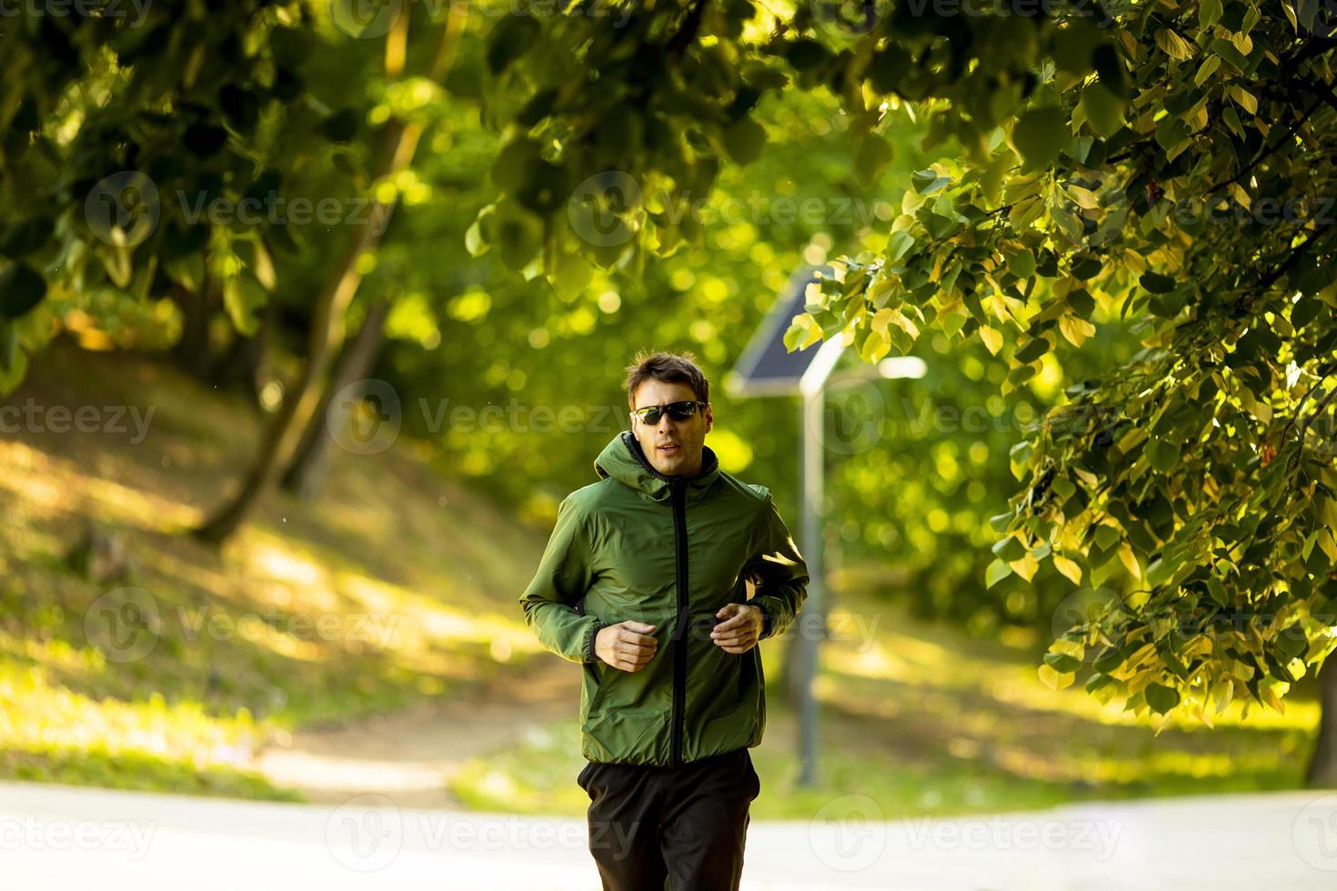 giovane atletico che corre mentre si allena nel soleggiato parco verde foto