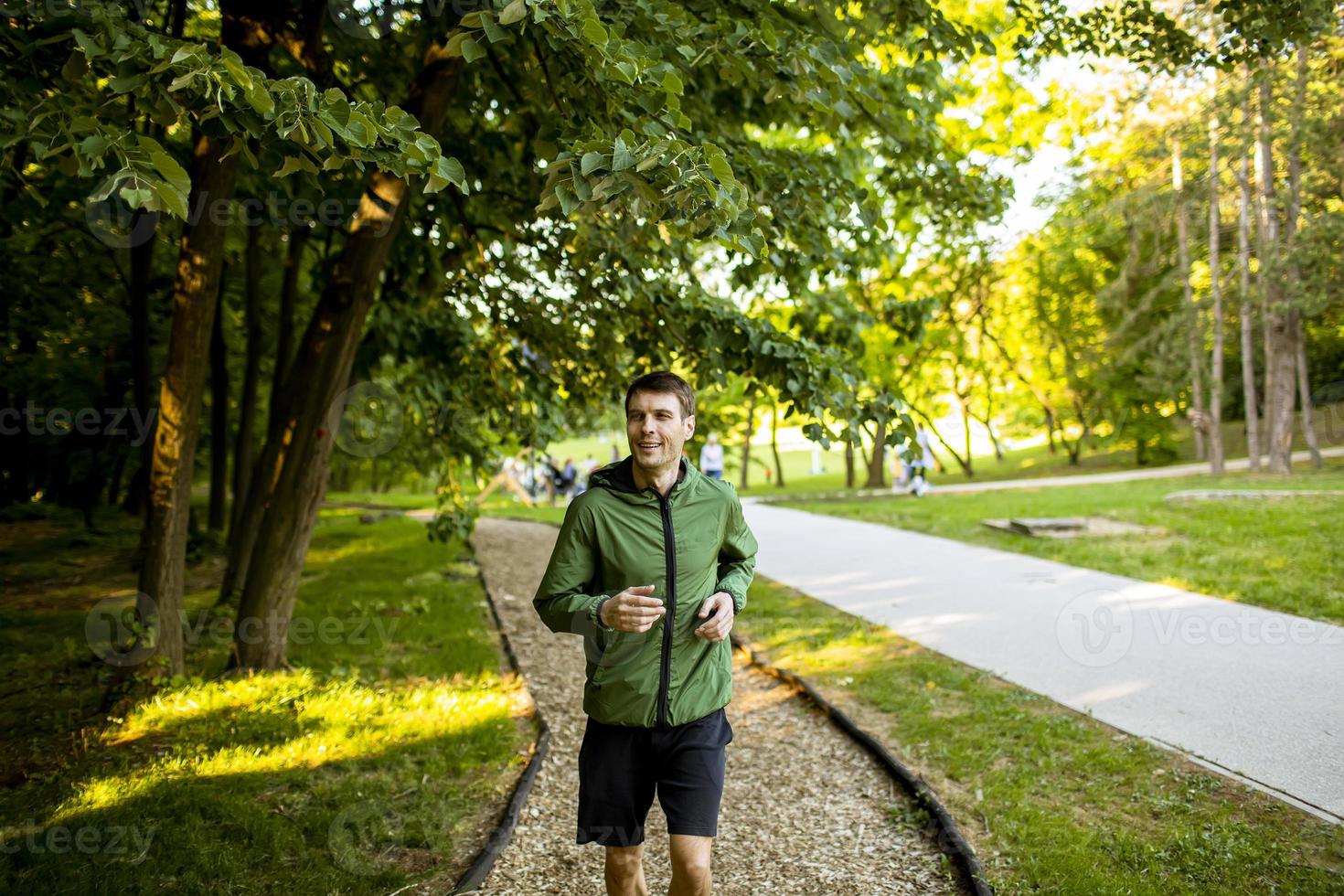 giovane atletico che corre mentre si allena nel soleggiato parco verde foto