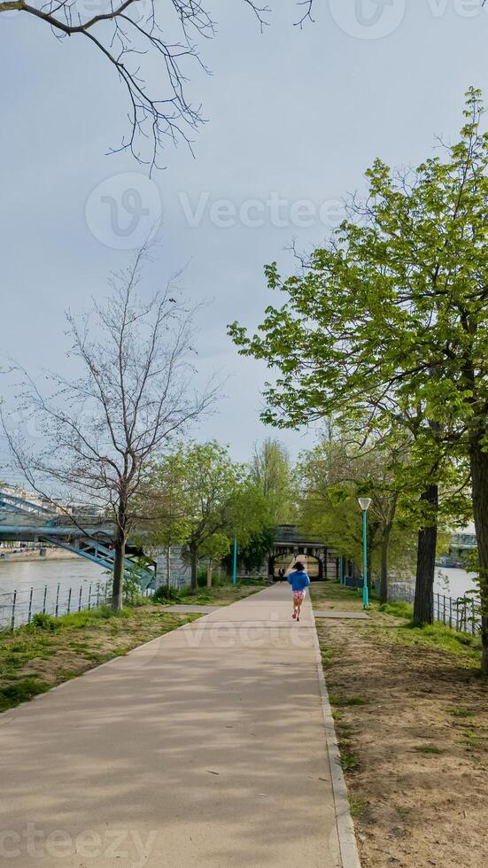 individuale jogging su un' tranquillo sul fiume sentiero nel molla, promozione fitness e terra giorno attività, in mezzo gemmazione alberi e chiaro cieli foto