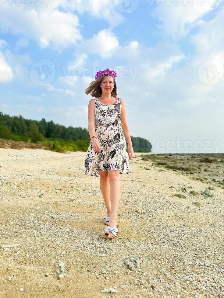 un' donna ornato con un' vivace fiore corona passeggiate con gioia lungo un' appartato spiaggia, indossare un' floreale vestire, sotto un' luminosa blu cielo, la creazione di un' immagine di estate beatitudine foto