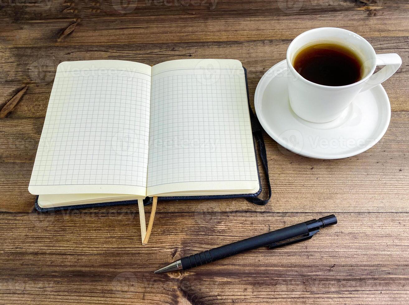 caffè nel un' tazza e un' taccuino con un' penna su un' di legno tavolo. foto