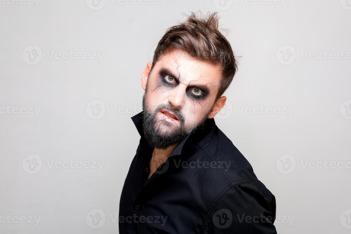un' barbuto uomo con in stile non morto trucco su Halloween sembra con grande occhi a il telecamera foto
