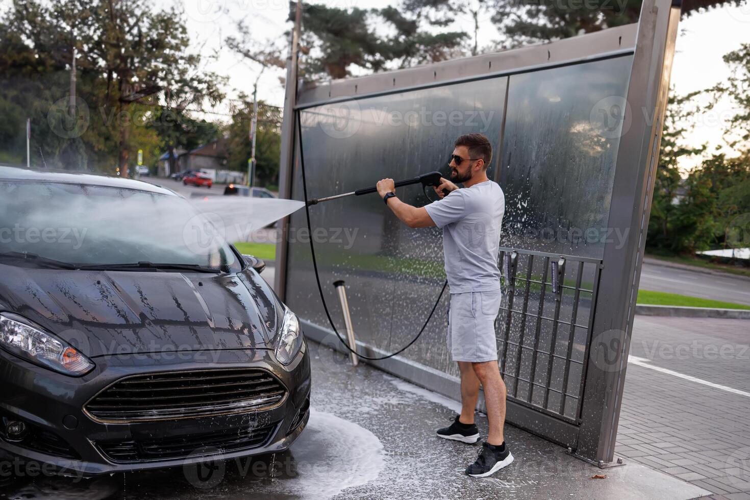 un' uomo a il auto lavare punti un' acqua cannone a il parabrezza. un' auto a un' se stesso servizio auto lavare. foto
