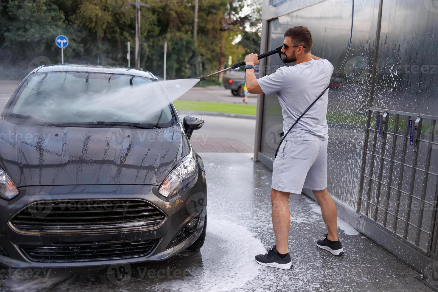 un' uomo punti un' acqua cannone a il parabrezza di un' macchina. un' auto a un' se stesso servizio auto lavare. foto