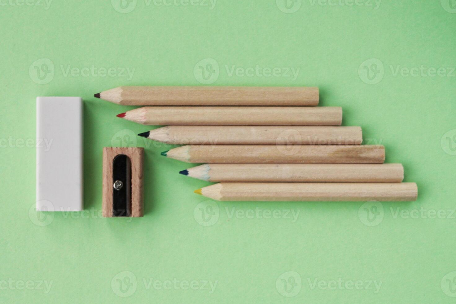 colorato matite, di legno Manuale temperamatite e gomma per cancellare su verde sfondo. indietro per scuola concetto. impostato di scrittura utensili per formazione scolastica, creatività, disegno, passatempo, arte. eco-friendly Stazionario foto