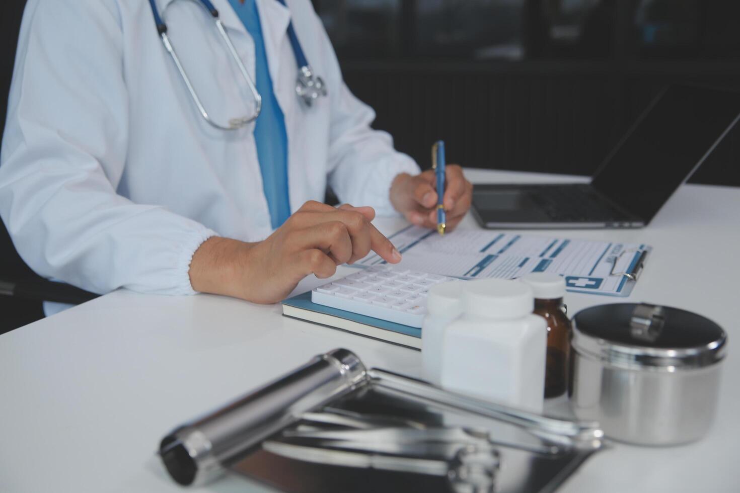 un' professionale e focalizzata asiatico femmina medico nel scrub è Lavorando e lettura medico ricerca su sua il computer portatile nel sua ufficio a un' Ospedale. foto