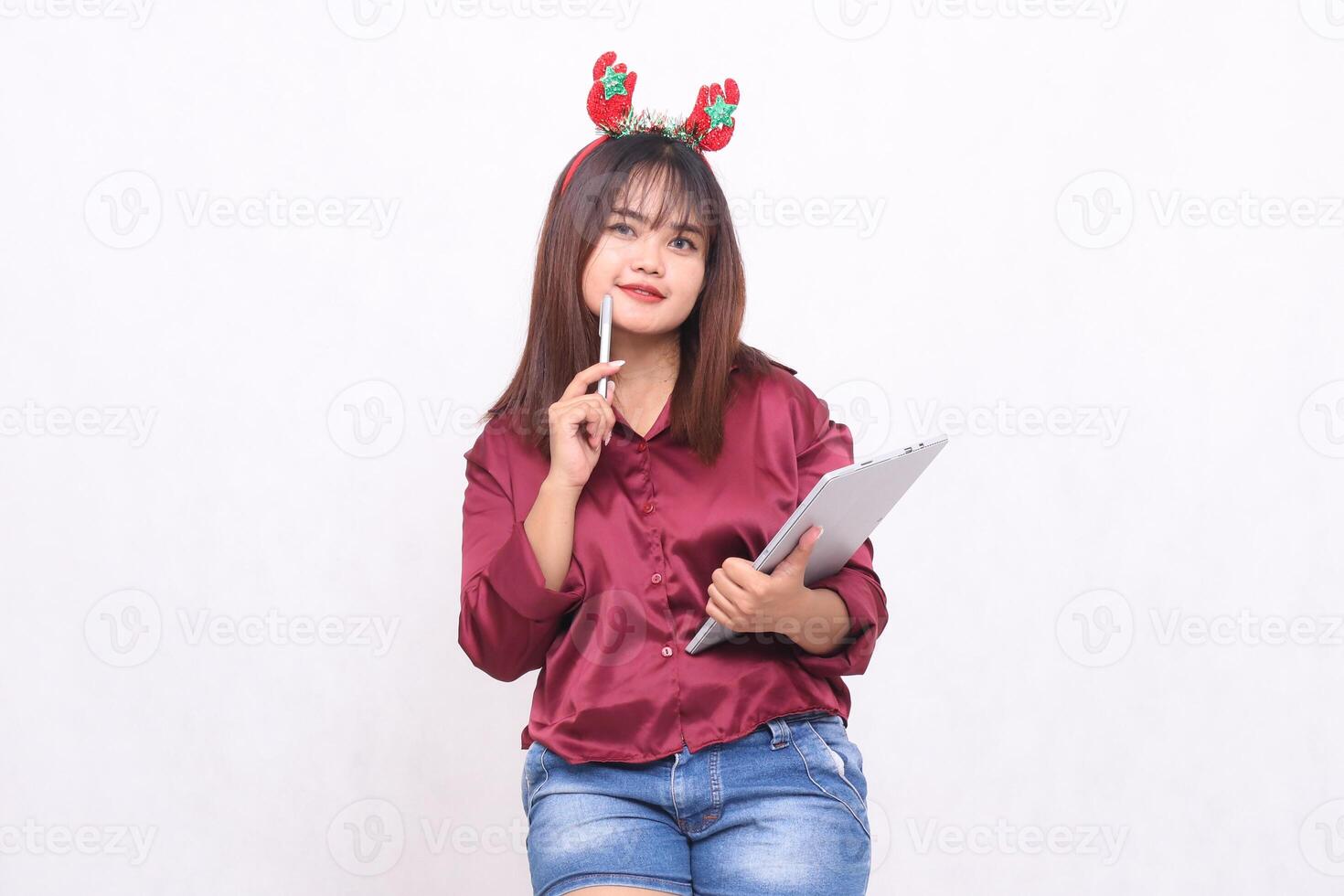 bellissimo giovane sud-est asiatico donna pensiero Tenere penna mentre trasporto il computer portatile tavoletta a Natale Santa Claus fascia per capelli indossare moderno rosso camicia bianca sfondo per promozione e pubblicità foto