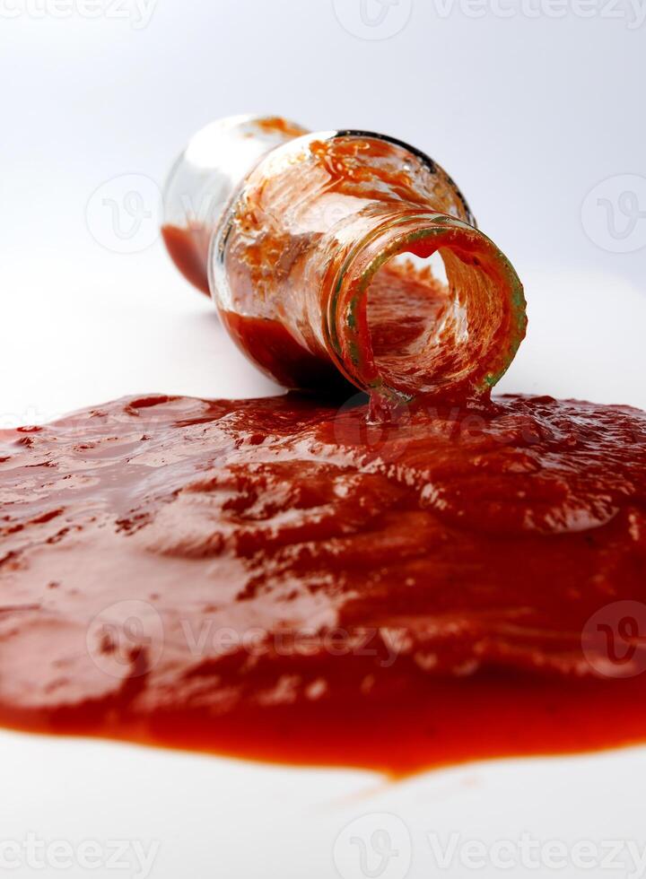 pomodoro salsa . un' bicchiere bottiglia con ketchup e un' pozzanghera di ketchup rovesciato in giro esso. foto