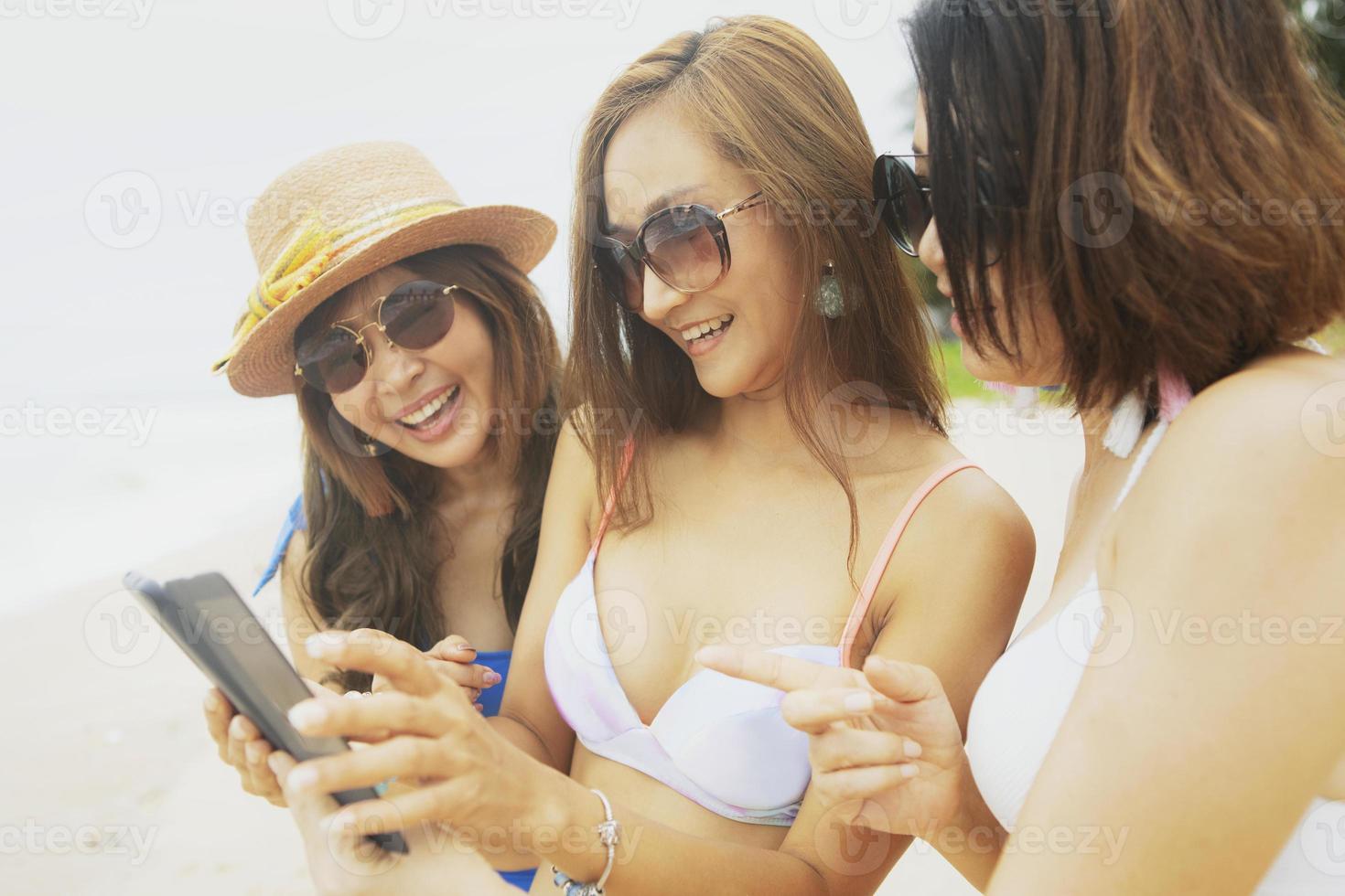 tre donne asiatiche che si rilassano sulla spiaggia estiva e si fanno selfie con lo smartphone foto