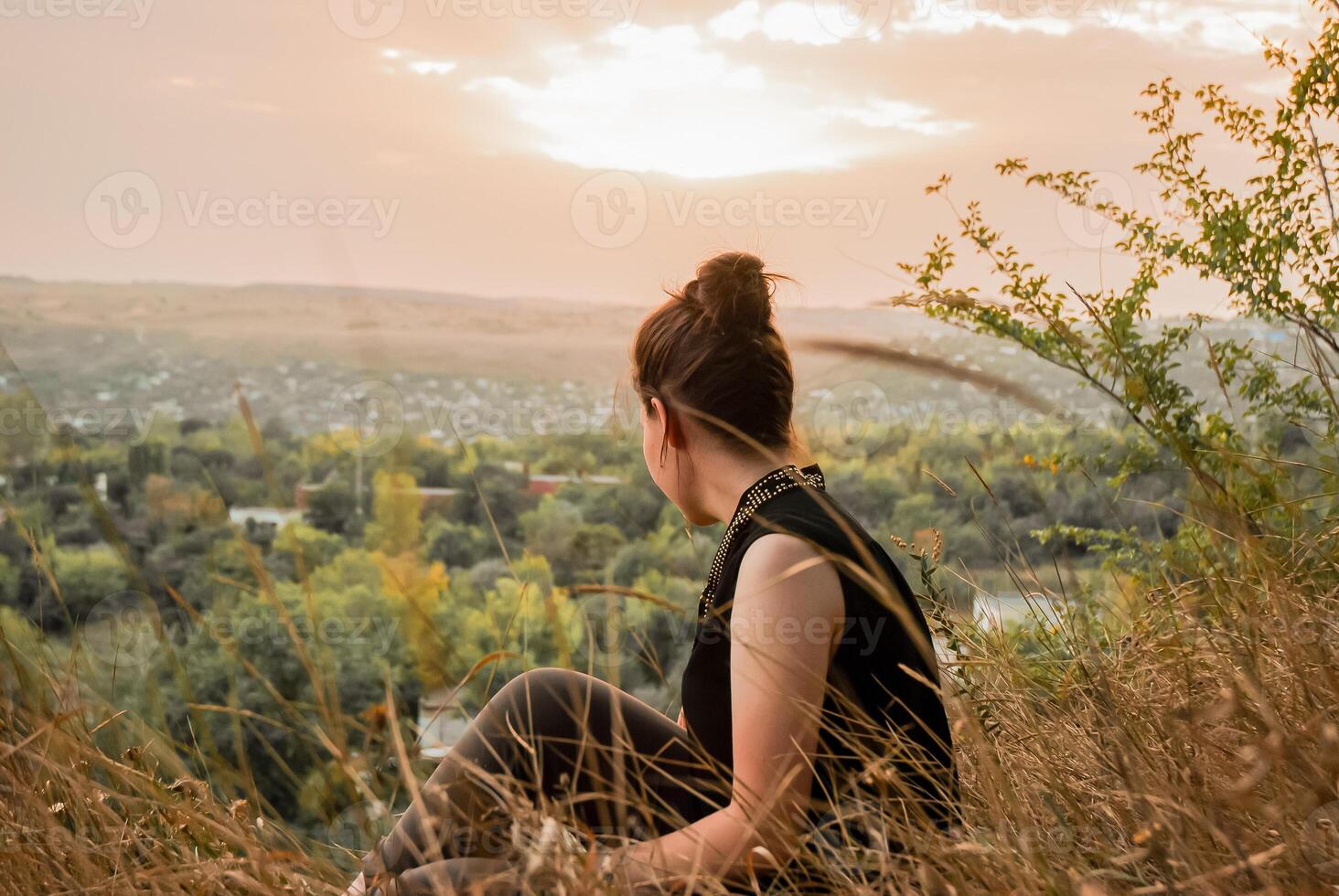 donna seduta su collina, godendo un' tranquillo tramonto al di sopra di un' campagna paesaggio, riflettendo su della natura serenità foto