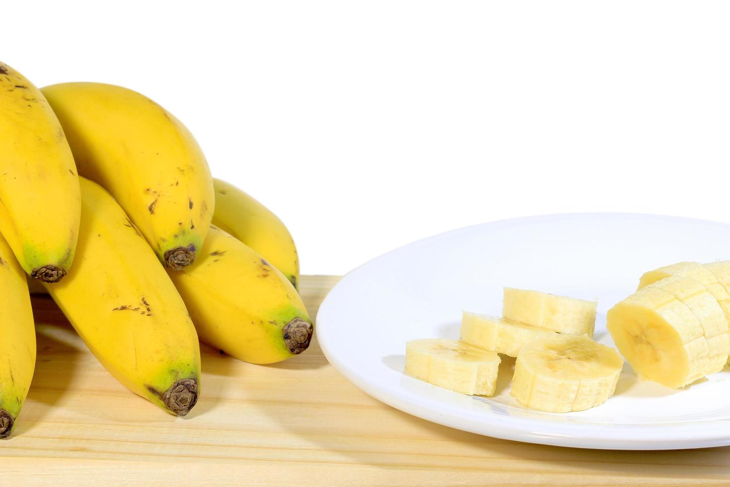 grappolo di banane sul tavolo di legno accanto al piatto con frutta a fette, sfondo bianco foto