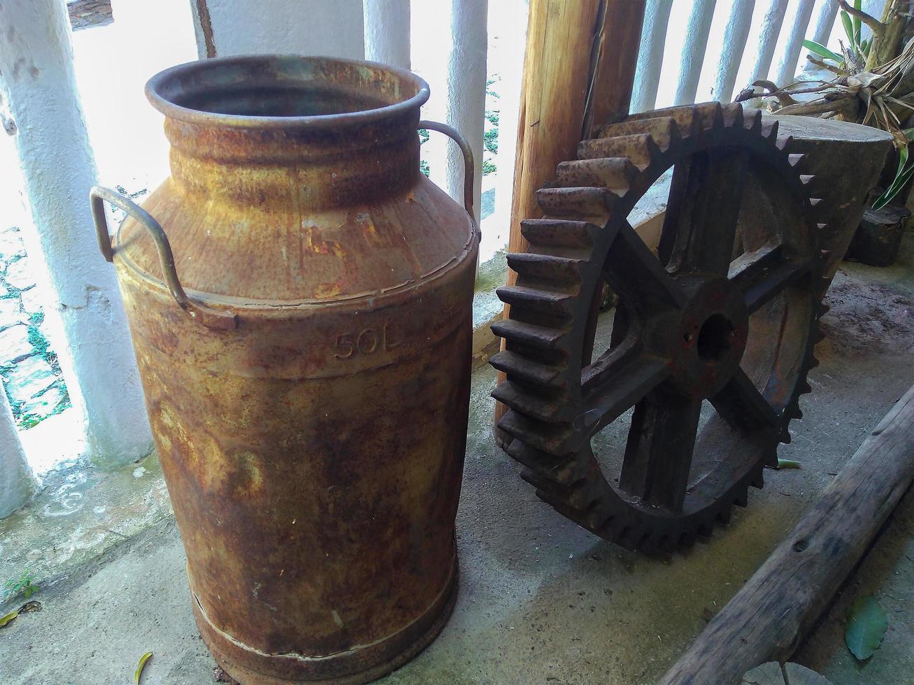 ottone latte d'epoca sul portico rustico della fattoria accanto all'ingranaggio del mulino ad acqua foto