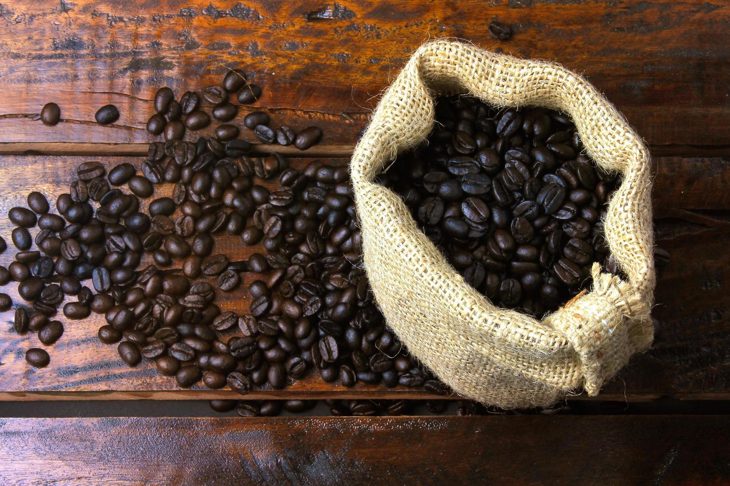 chicchi di caffè tostati e freschi all'interno di un sacchetto di tessuto rustico e versati su un tavolo in legno rustico foto