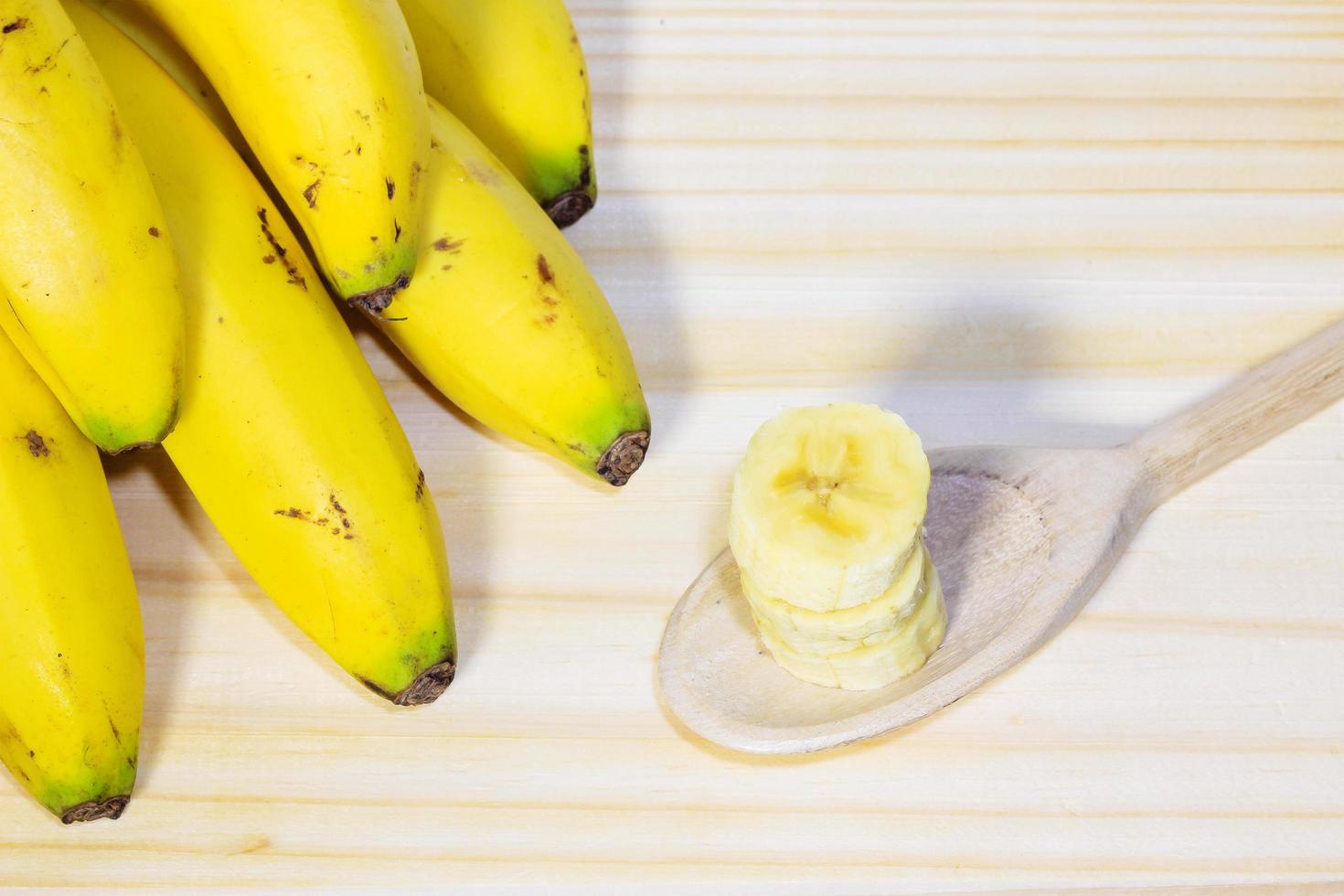 grappolo di banane sul tavolo di legno accanto al cucchiaio con frutta a fette foto