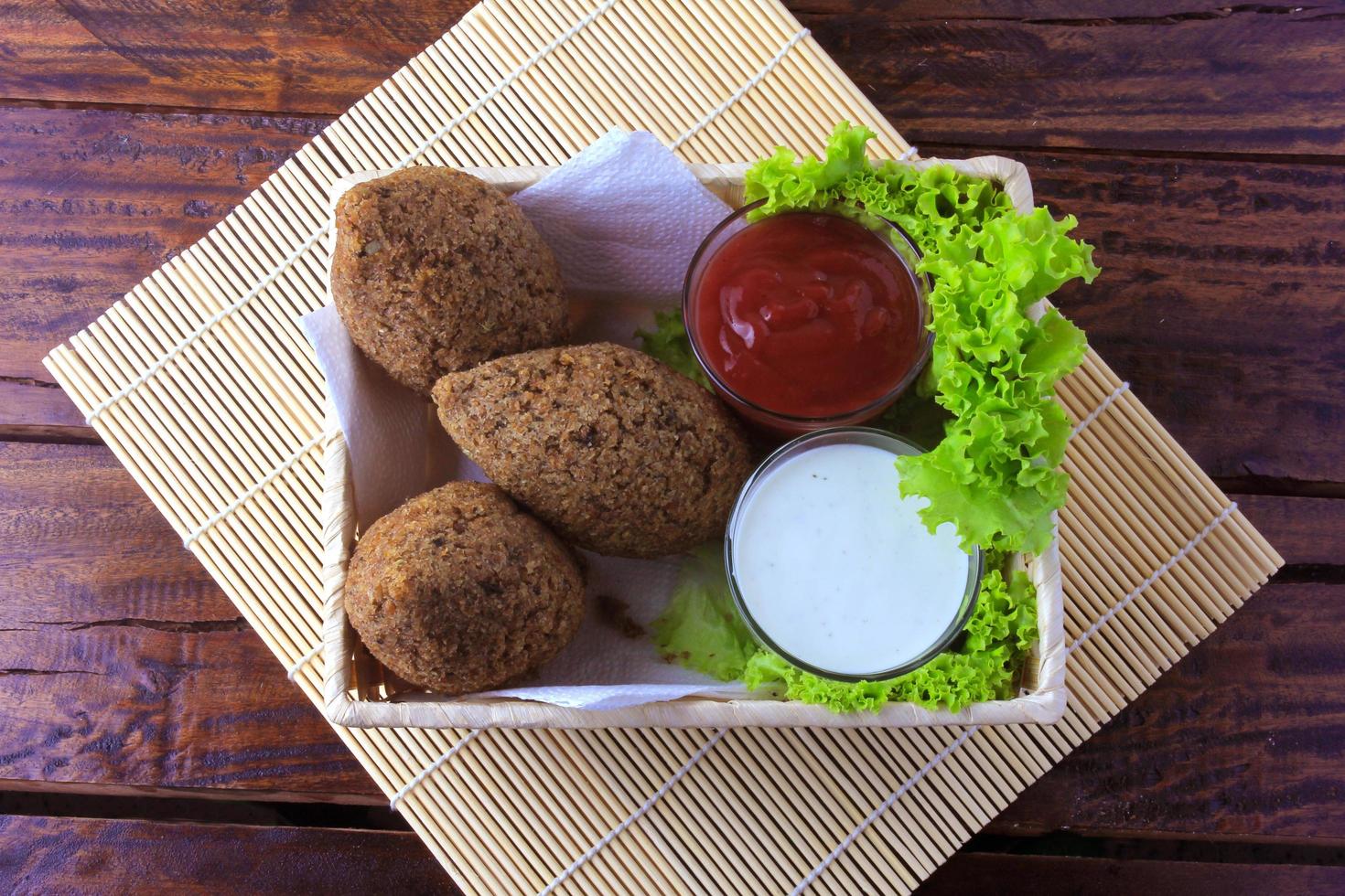 Kibbeh fritto con salsa di pomodoro in un cestello, su tavola in legno rustico foto