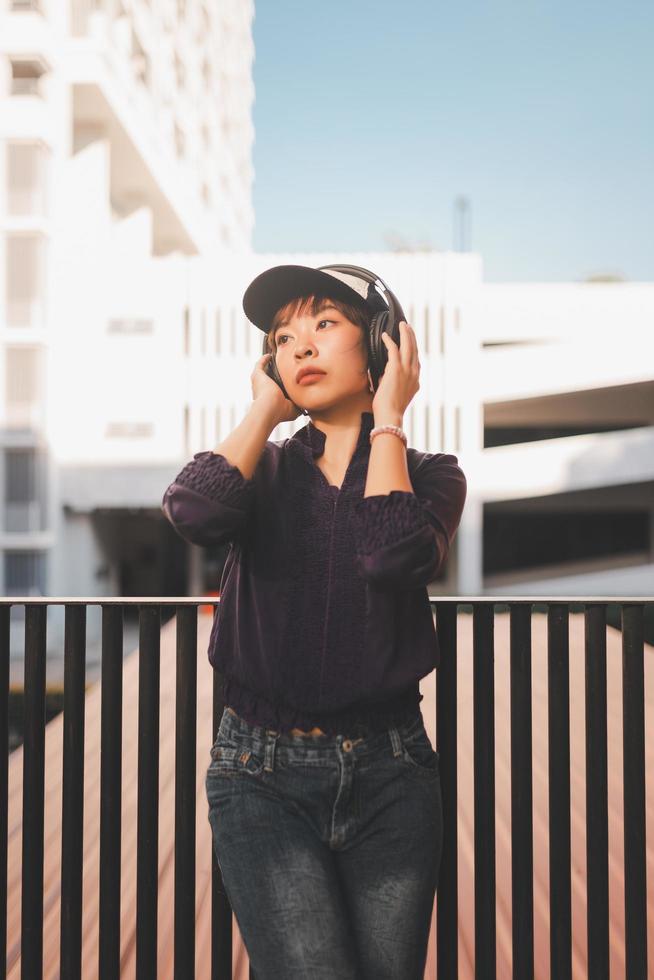 felice giovane donna asiatica che ascolta musica e si diverte con le cuffie per strada foto