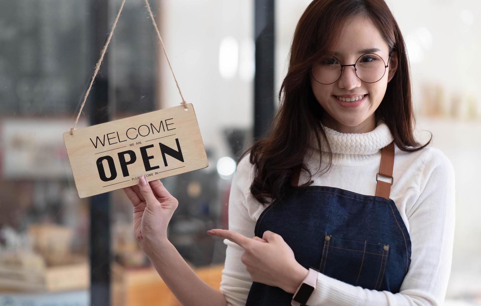 avvio successo piccolo imprenditore PMI bellezza ragazza stand mano tenere aperto segno caffetteria ristorante. ritratto di giovane donna asiatica abbronzata proprietario di un barista caffè. banner del concetto di business dell'imprenditore di PMI foto