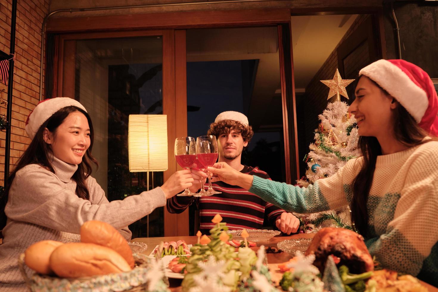 la famiglia e gli amici della felicità stanno festeggiando, alzando i bicchieri e un sorriso allegro con le bevande, si divertono a mangiare cibi nella sala da pranzo di casa, decorati per la festa di Natale e il giorno di capodanno. foto