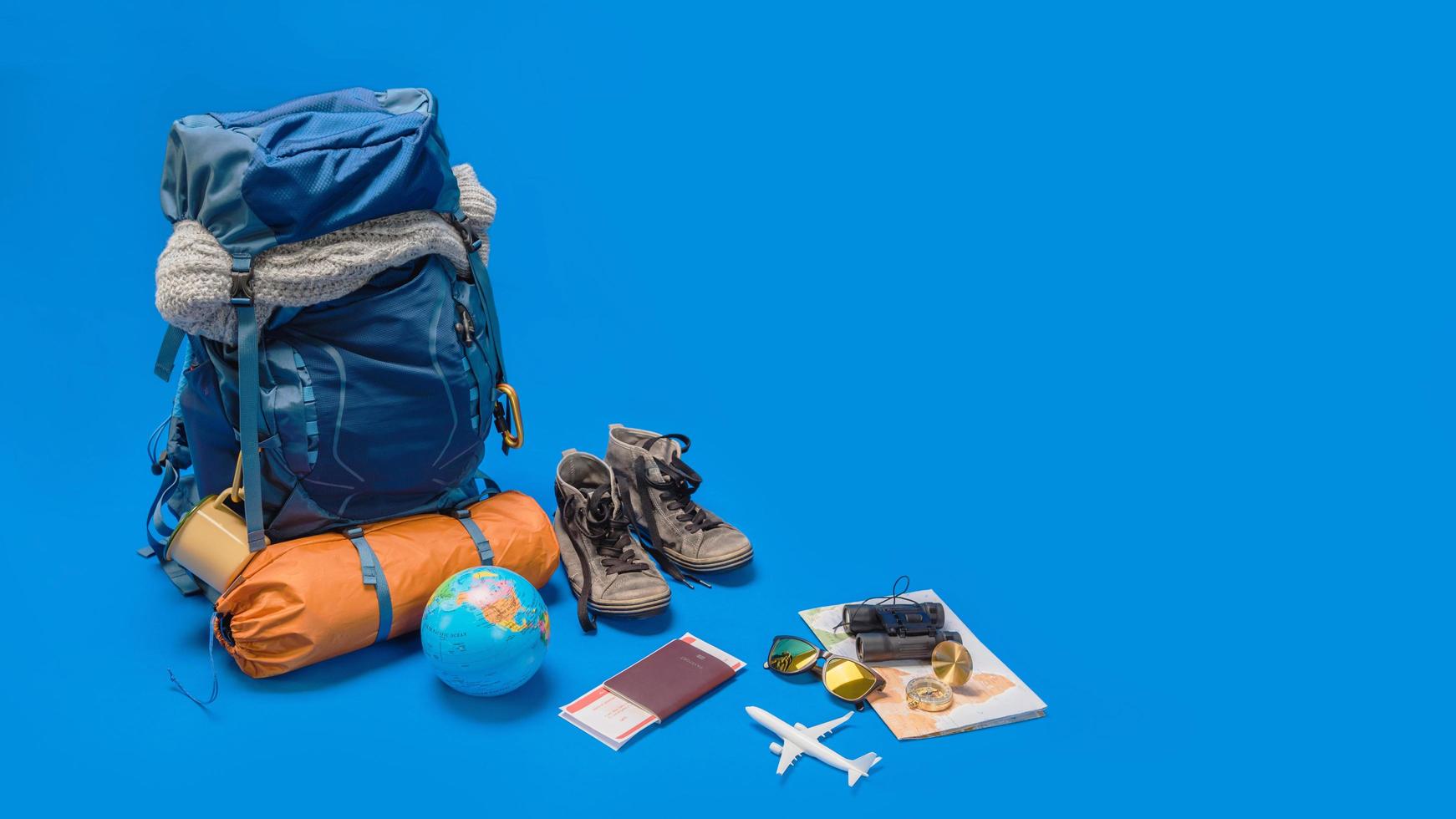 il concetto di organizzazione dell'attrezzatura per il viaggio messo sui bagagli. accessorio di concetto per le vacanze dei viaggiatori con una mappa, passaporto su sfondo di colore blu. zaino da viaggio foto