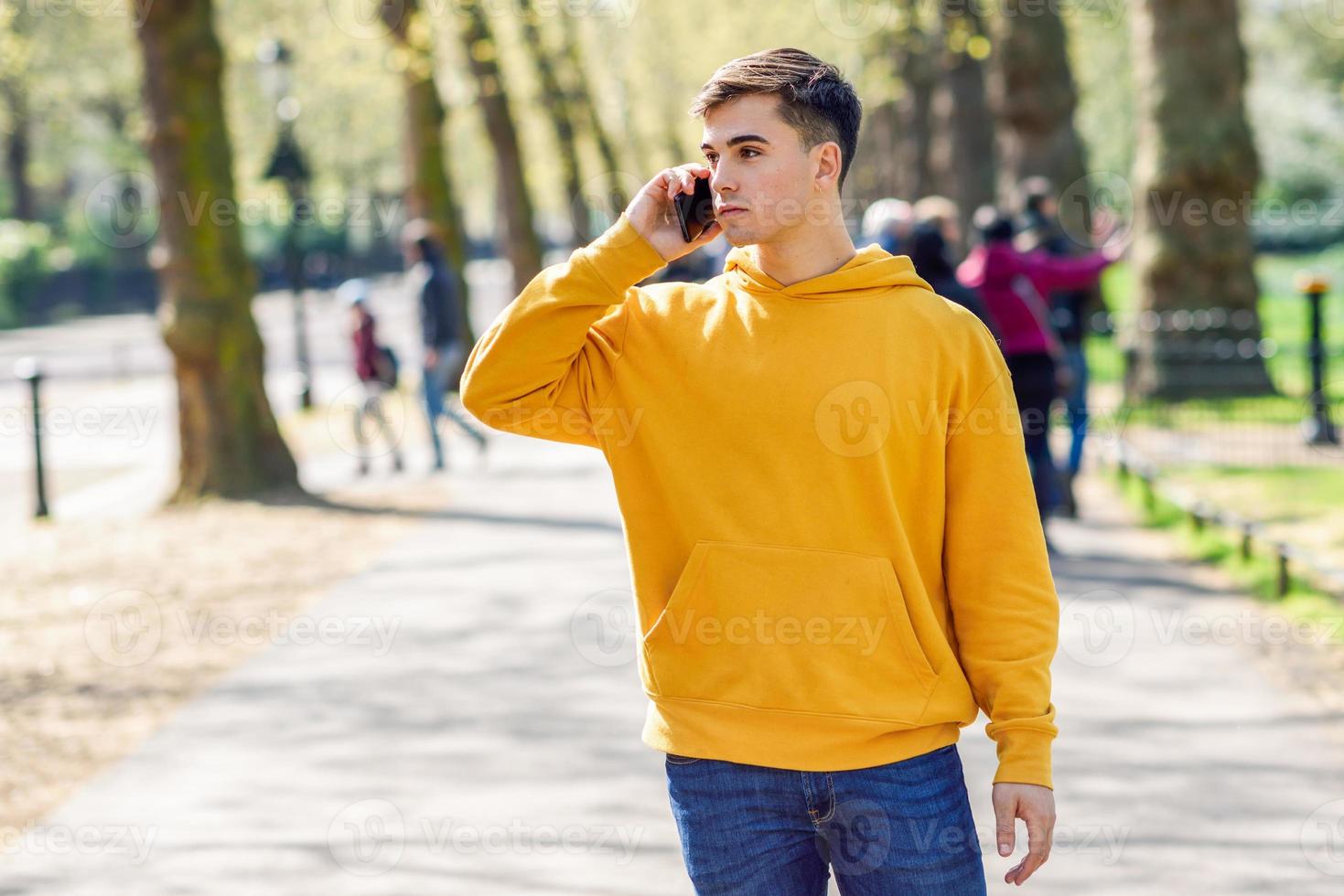 giovane uomo urbano che utilizza smartphone camminando in strada in un parco urbano a Londra. foto