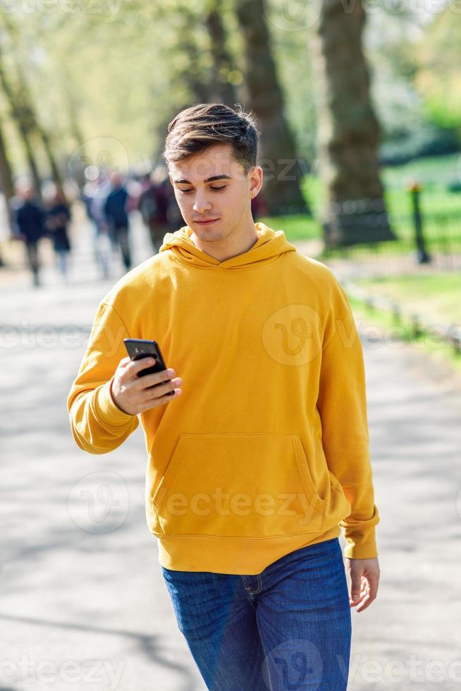 giovane uomo urbano che utilizza smartphone camminando in strada in un parco urbano a Londra. foto