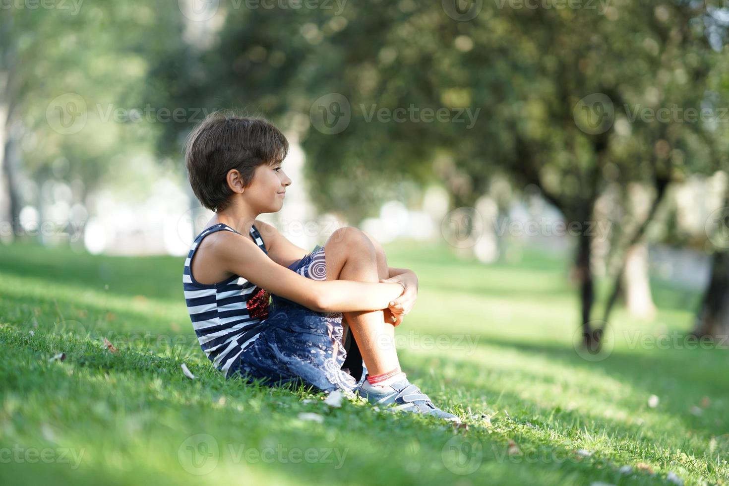 bambina, otto anni, seduta sull'erba all'aperto. foto