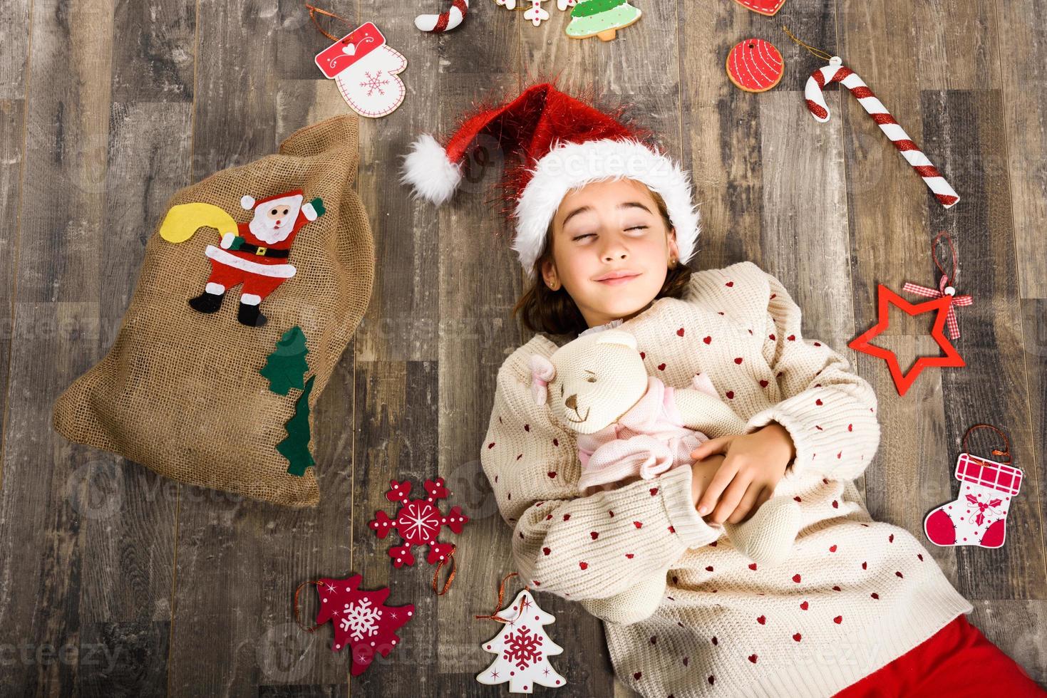 adorabile bambina che indossa un cappello da Babbo Natale sdraiato sul pavimento di legno foto