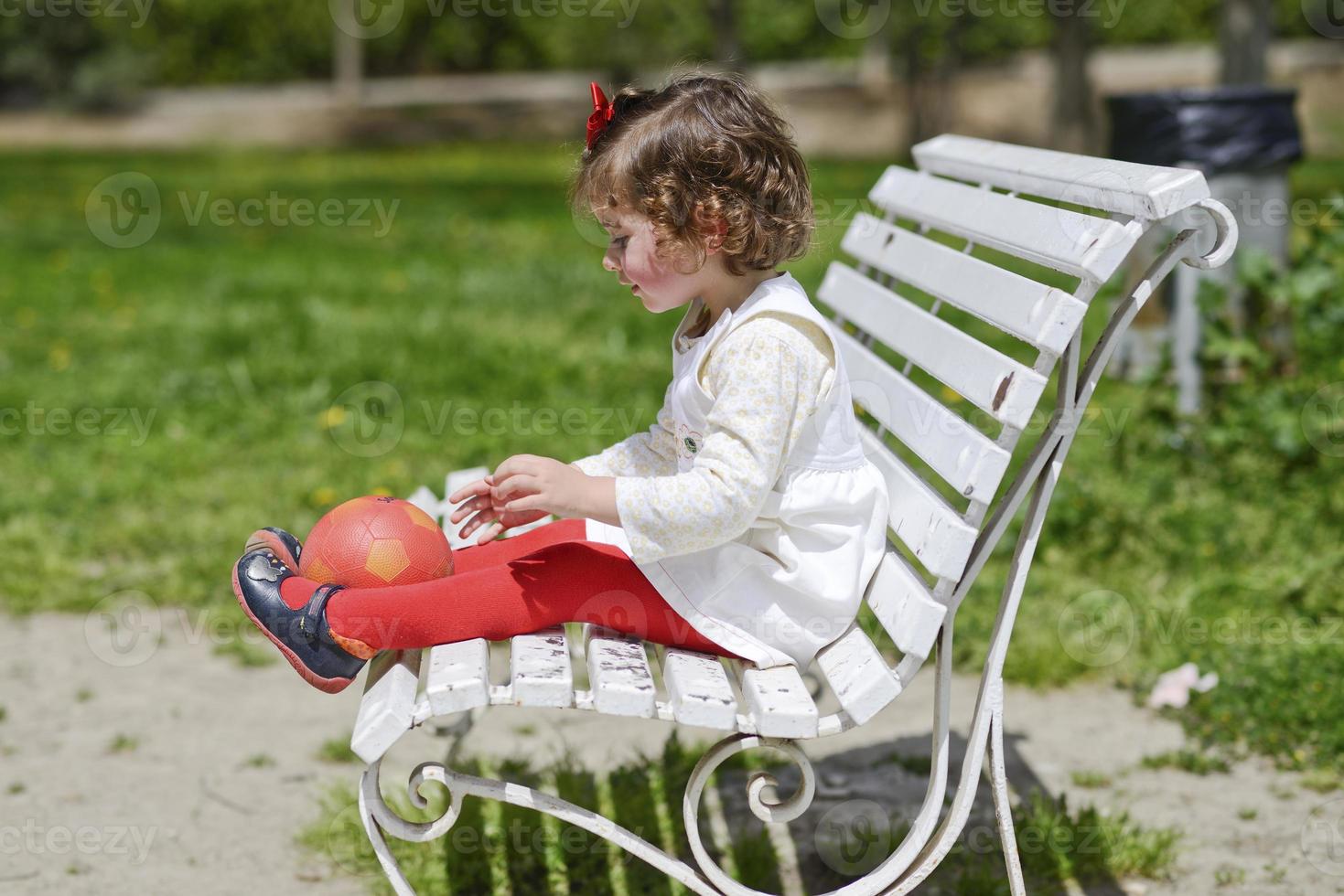 bambina che gioca con una palla seduta su una panchina del parco. foto