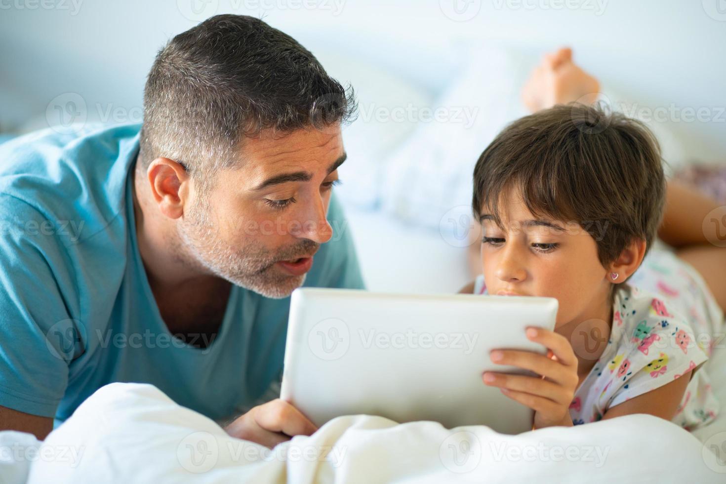 padre di mezza età con sua figlia di otto anni che utilizza tablet digitale in camera da letto. foto